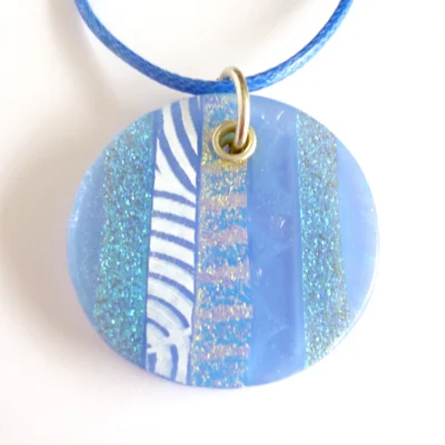Large blue dichroic glass pendant with a blue cord on a white background