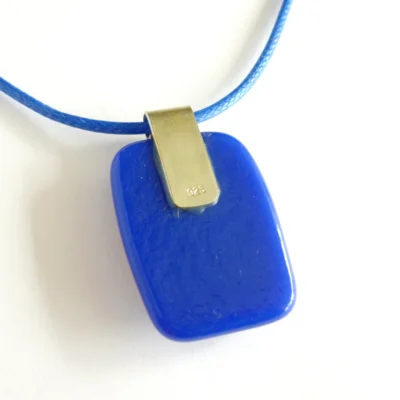 The back of blue fused glass pendant with 925 sterling silver bail and blue cord.