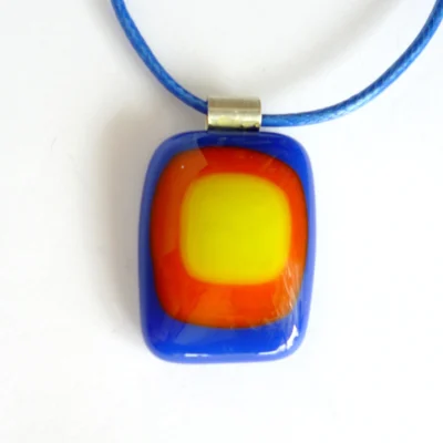 A handmade blue, red and yellow stacked fused glass pendant attached to a blue cord, emphasising its unique and eye-catching style
