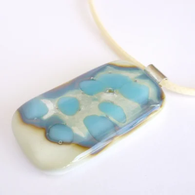 Oblong cream pendant with turquoise, silver and an outline of brown. 925 sterling silver bail attached and hangs from a cream cord necklace.