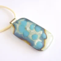 Cream silver and blue fused reactive glass pendant hanging from a cord necklace.