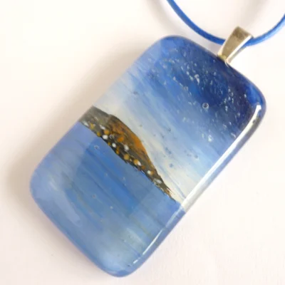 Fused glass seascape pendant, with sky, sea and hill in the distance. Sterling silver bail and cord necklace attached