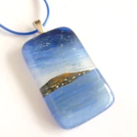 Blue fused glass seascape pendant laying at an angle on a white background
