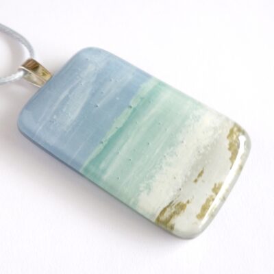 Fused glass seascape pendant laying on a white background