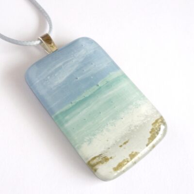 Handmade and hand-painted fused glass seascape pendant with sea, sky and sand. Sterling silver bail and grey cord attached.