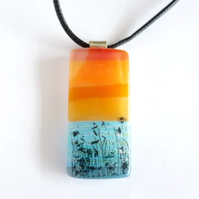 Front view of seascape orange and blue fused glass pendant.