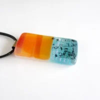 Side view of orange and blue seascape fused glass pendant with sterling silver bail and black cord necklace.