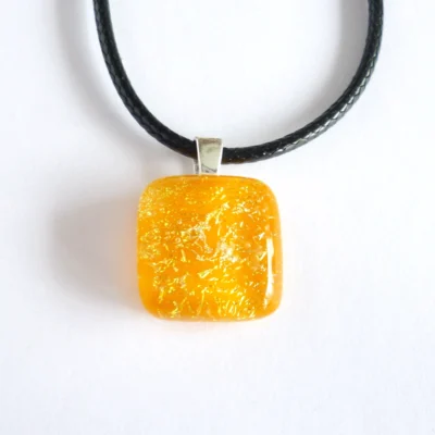 Front view of dichroic glass pendant with sterling silver bail and cord necklace laying on a white background