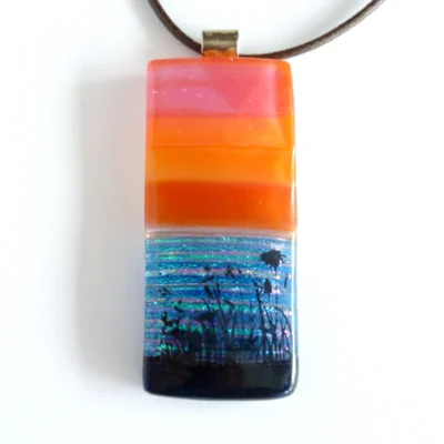Orange fused glass pendant with a seascape scene and black decal flowers and grass. Sterling bail and brown cord necklace