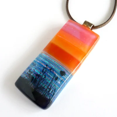 Fused glass pendant with seascape scene laying at an angle on a white background