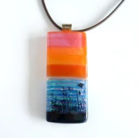 Oblong fused glass pendant in different shades of orange with dichroic for shimmering water. Sterling silver bail and brown cord