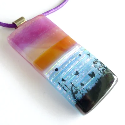 Seascape fused glass pendant in pink / purple and tan with sterling silver bail. Dichroic ripples for water with black butterfly and grass design printed on top. Hangs from a purple cord necklace.