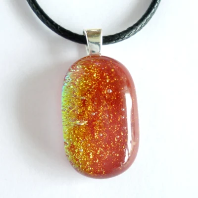 Handmade red dichroic glass pendant with sterling silver bail and hanging from a black cord necklace