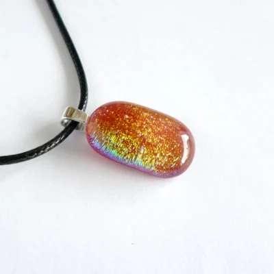 Side view of red fused dichroic glass pendant with sterling silver bail and black cord necklace