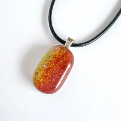 Dichroic glass pendant necklace laying at an angle on a white background.