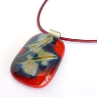 Red fused reactive glass pendant at an angle on white background
