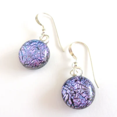 Pink dichroic glass earrings laying at an angle on a white background. Crackle effect dichroic glass cabochons attached to silver plated bails and sterling silver ear hooks.