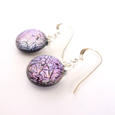 Pink dichroic earrings laying at an angle showing depth of glass. Silver plated bails and sterling silver hooks attached.