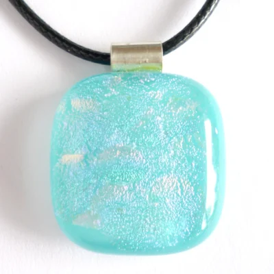 Close up of shimmering turquoise blue dichroic glass pendant with colours of pink and blue, hanging from a black cord necklace.