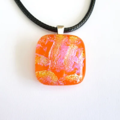 Front view of dichroic glass pendant showing yellow/orange and pink shimmers hanging from a black cord necklace.