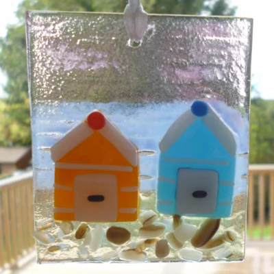 Fused glass coastal suncatcher hanging in a window, showing light shining through.