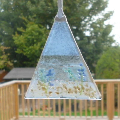 Single triangle shaped fused glass coastal suncatcher with blue flowers and hanging from a white ribbon.