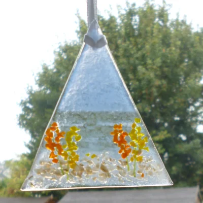 Single triangle shaped fused glass coastal suncatcher with orange and yellow flowers and hanging from a white ribbon.