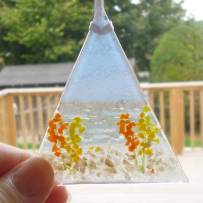 Triangle shaped fused glass coastal suncatcher being held at one angle showing size.