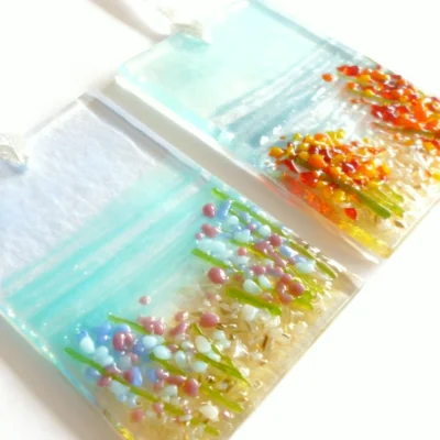 Two fused glass coastal suncatchers laying on a white background at an angle showing detail of the glass.
