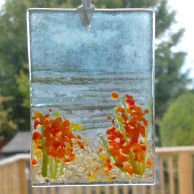 Small rectangle fused glass coastal suncatcher with flowers hanging from a white ribbon in a window.