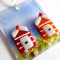 Small fused glass coastal suncatcher laying at an angle showing detail of red and orange beach huts, hanging from a white ribbon.