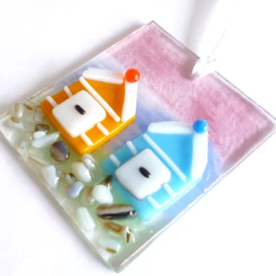 Fused glass coastal suncatcher laying at an angle showing detail of orange and blue beach huts with white stripes.