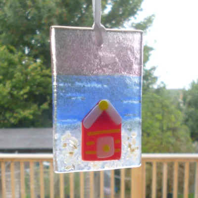 Rectangle shaped fused glass suncatcher with beach hut hanging in a window.