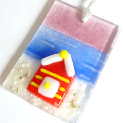 Fused glass suncatcher laying at a slight angle showing detail of beach hut. Hangs from a white ribbon.