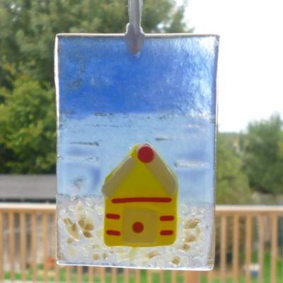 Small fused glass suncatcher with a yellow beach hut hanging in a window.
