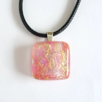 Front view of pendant with sterling silver bail and black cord attached.. Shimmers of pink and yellow / gold seen in the dichroic glass.