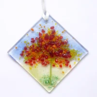 Diamond shaped autumn colours fused glass suncatcher hanging from a white ribbon. Tactile glass, in colours of red, orange and green.