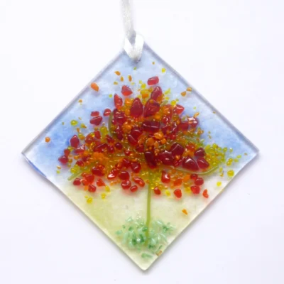 Diamond shaped autumn colours fused glass suncatcher hanging from a white ribbon. Tactile glass, in colours of red, orange and green.