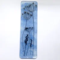 Blue fused glass dandelion suncatcher. Blue background created by copper oxide and dandelion made using very thin black stringers, similar to a pencil drawing. Hangs from a clear cord.