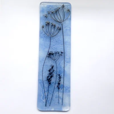 Blue fused glass dandelion suncatcher. Blue background created by copper oxide and dandelion made using very thin black stringers, similar to a pencil drawing. Hangs from a clear cord.
