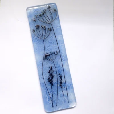 Unique blue fused glass dandelion suncatcher laying at a slight angle.
