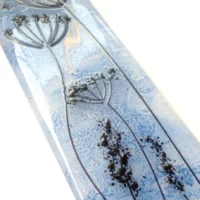 Close up of outline of fused glass dandelion. Background blue with black stringer design.