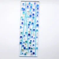 Fused glass suncatcher with blue glass beads fused on top. Clear glass with blue, turquoise and dichroic glass beads and stringers fused on top of a clear piece of glass.