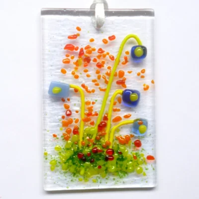 Rectangle blue glass flower suncatcher, with red and orange frit for decoration. Quirky square flowers with stringer stems. Hangs from a white ribbon.