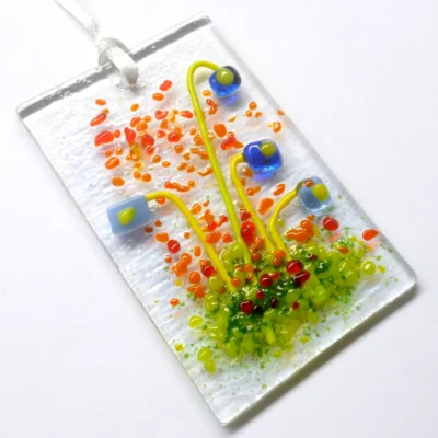 Rectangle blue glass flower suncatcher with quirky square flowers. Suncatcher laying at a slight angle with white ribbon attached.