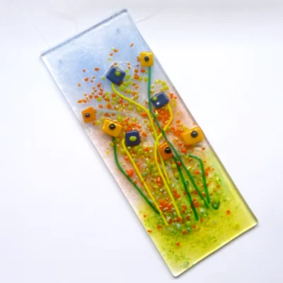 Blue and orange glass flower suncatcher laying at a slight angle on a neutral background.