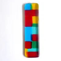 Long slim handmade fused glass suncatcher with blocks of colour in red, yellow, blue and green. Hold drilled at the top with a clear wire threaded through to hang from.