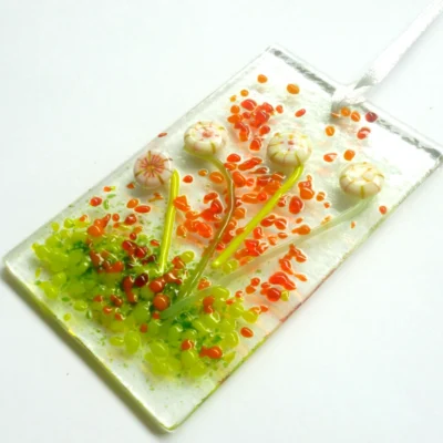Cream glass flower suncatcher laying at a slight angle hanging from a white ribbon.