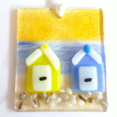 Small square yellow and blue fused glass coastal suncatcher hanging from a ribbon. White trim for doors and roof, with frit for stones at the bottom.