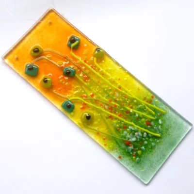 Fused glass floral suncatcher featuring quirky green square flowers on long stems with orange and green frit laying at an angle.
